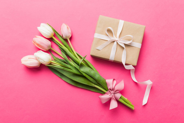 Pink tulips flowers and gift or present box on colored table background. Mothers Day, Birthday, Womens Day, celebration concept. Space for text top view. - Foto, imagen