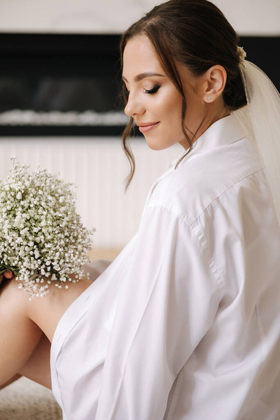Нежная невеста с красивым свадебным букетом, одетая в рубашку жениха. Высокое качество фото - Фото, изображение