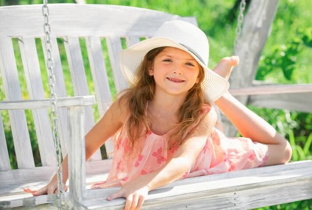 Child dreaming. Happy child girl laughing and swinging on a swing at the park in summer. Kids happiness and smile. Close up portrait of a beautiful child girl in hat dreaming. Dreamy kids face - Photo, image