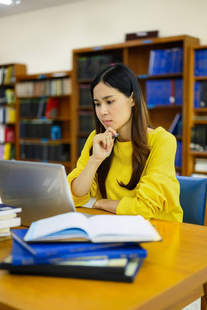 Gerichte vrouwelijke universitaire student doet onderzoek naar laptop, leerlessen, voorbereiding van examens in de bibliotheek. - Foto, afbeelding
