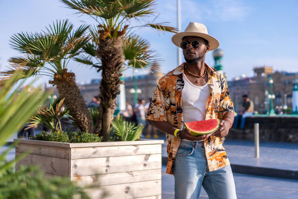 Portrait of a black ethnic man enjoy summer vacation on the beach, shade and a watermelon smiling - Photo, Image