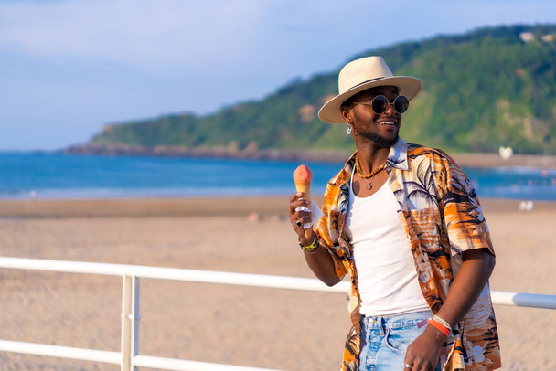 Black ethnic man enjoy summer vacation on the beach eating an ice cream enjoying strolling - Фото, зображення