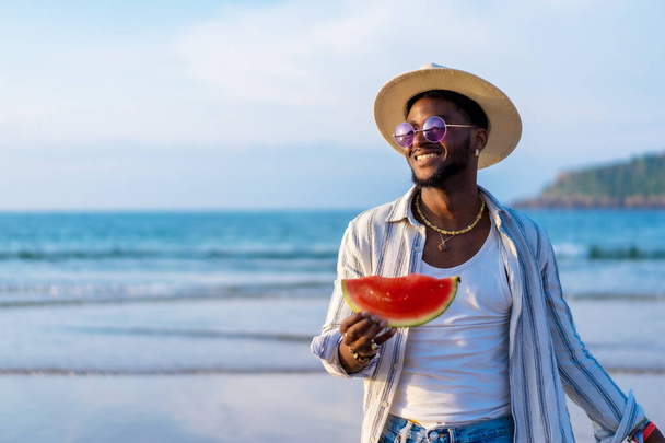Portrait of a black ethnic man enjoy summer vacation at the beach eating a watermelon - Foto, Imagem