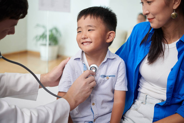 Smiling boy looking at doctor listening to his breath, visiting pediatrician concept - Фото, зображення
