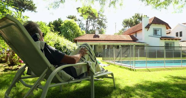 Senior man resting by pool lying down and relaxing in backyard home - Foto, Imagem