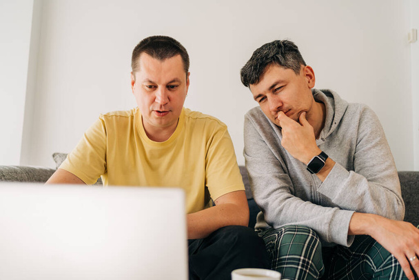 Two IT freelancer men typing in laptop working from home office. Two programmers sitting on couch doing code review. Distance learning online education and work. - Photo, Image