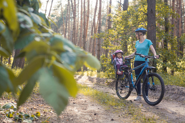 mother with small baby on bicycle. Family biking in the summer pine forest - Photo, image