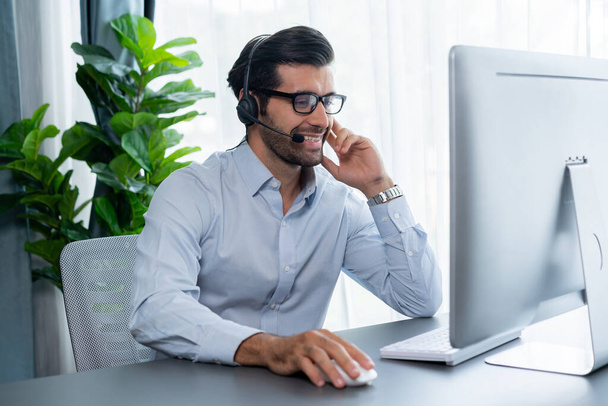 Male call center operator or telesales representative siting at his office desk wearing headset and engaged in conversation with client providing customer service support or making a sale. fervent - Photo, Image