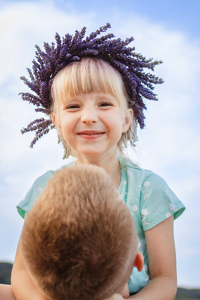 Happy little girl in a lavender crown on dads arms. father holding daughter - Фото, зображення