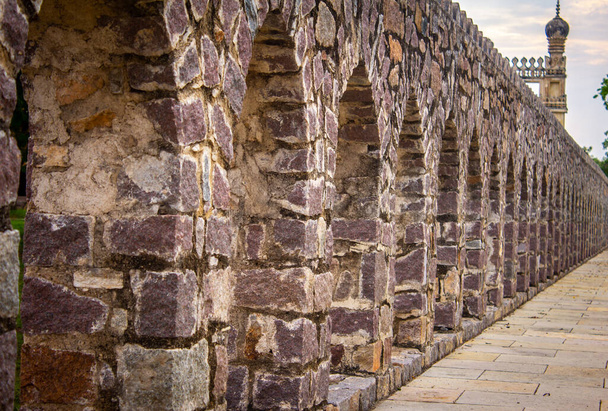 Corredor construído com pedras entre as estruturas tumulares e o jardim paisagístico no Parque Arqueológico Qutb Shahi, Hyderabad, Índia - Foto, Imagem