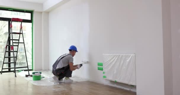 Man in handschoenen met verf roller verf muur. Kunstenaar schildert muur van huis met roller en witte verf - Video