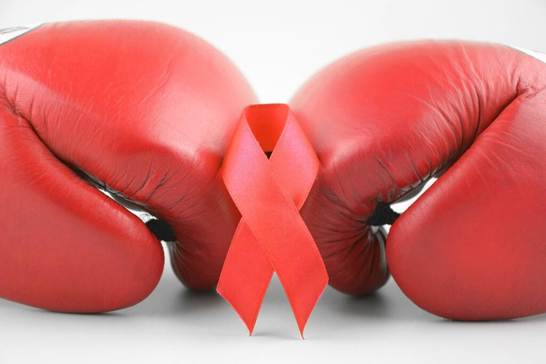 Ruban rouge avec gants de boxe, symbole de lutte. Journée mondiale du sida et Mois national de la sensibilisation au VIH, au sida et au vieillissement. - Photo, image
