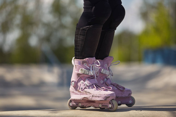 Aggressive inline skater girl wearing purple skates. Feet of female roller blader in outdoor skatepark in summer - 写真・画像