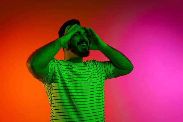 Portrait of bearded man in striped shirt posing with calm, positive face against gradient studio background in neon light. Concept of human emotions, facial expression, lifestyle, success - Foto, Imagem