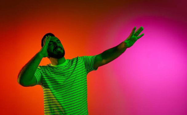 Portrait of bearded man in striped shirt posing with calm, positive face against gradient studio background in neon light. Concept of human emotions, facial expression, lifestyle, success - 写真・画像