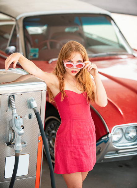 Sexy Retro Girl with Car. Gas station, woman refuel the auto. Red retro automobile - Фото, изображение
