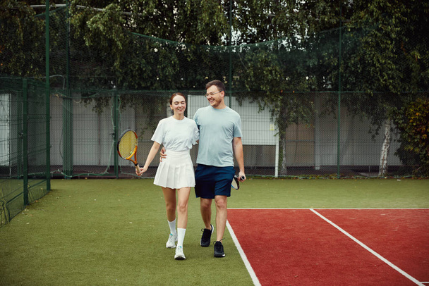 Young couple on tennis court. Two tennis players are smiling and walking around the court and talking - Φωτογραφία, εικόνα