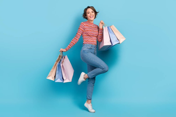 Full length photo of sweet excited lady wear striped top walking rising shoppers isolated blue color background. - Фото, изображение