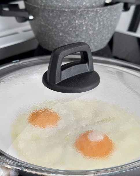 fried eggs in a frying pan under a transparent glass lid - Foto, Bild