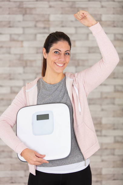 thoughtful fitness woman holding weight scale - Foto, imagen