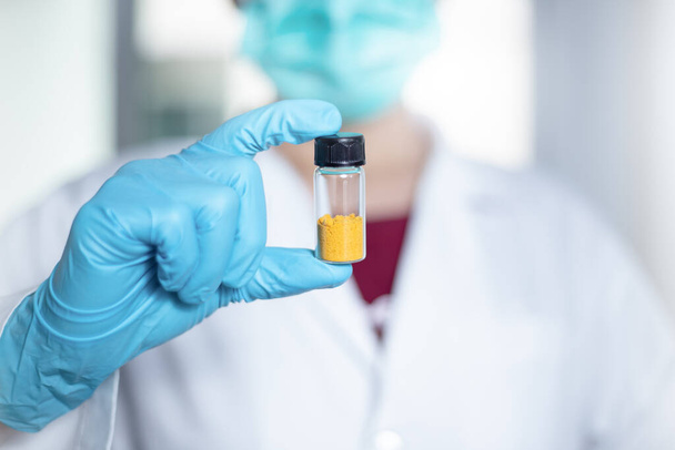 Scientist woman shows an orange solid in a vial glass of curcumin compound from extraction and isolation in the laboratory. Curcumin substances are used for pharmaceuticals, medicine. - Foto, afbeelding