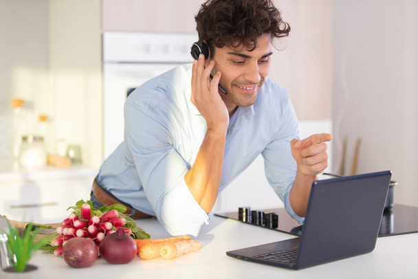 man in modern kitchen wearing headset and using laptop - 写真・画像