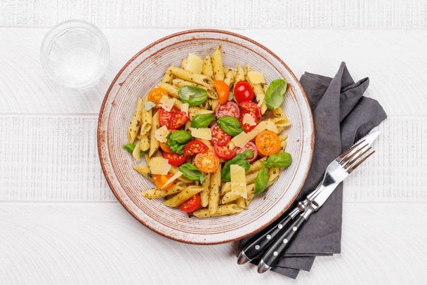 Un delicioso plato de pasta italiana adornada con tomates frescos y hojas aromáticas de albahaca. Puesta plana - Foto, imagen
