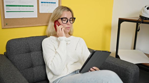 Fiatal szőke nő üzleti dolgozó beszél okostelefon segítségével touchpad az irodában - Fotó, kép