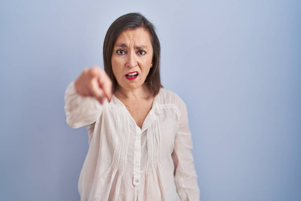 Middle age hispanic woman standing over blue background pointing displeased and frustrated to the camera, angry and furious with you  - Valokuva, kuva