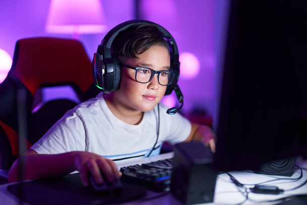 Adorable hispanic boy streamer playing video game using computer at gaming room - Foto, imagen