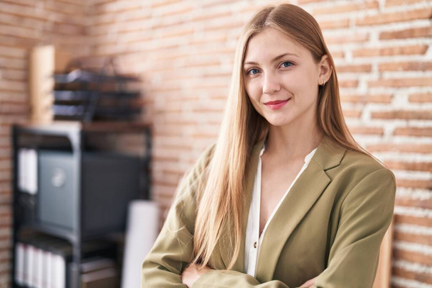 Young caucasian woman business worker standing with arms crossed gesture at office - Foto, afbeelding