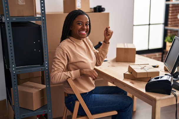 Young african american with braids working at small business ecommerce screaming proud, celebrating victory and success very excited with raised arm  - Photo, Image
