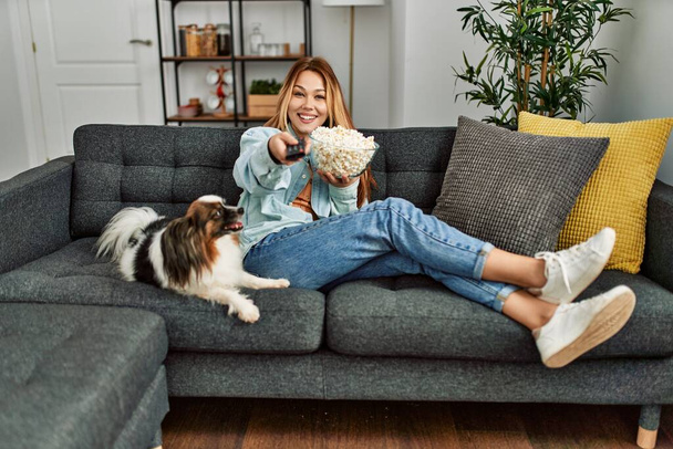 Junge kaukasische Frau sieht Film zu Hause auf Sofa mit Hund - Foto, Bild