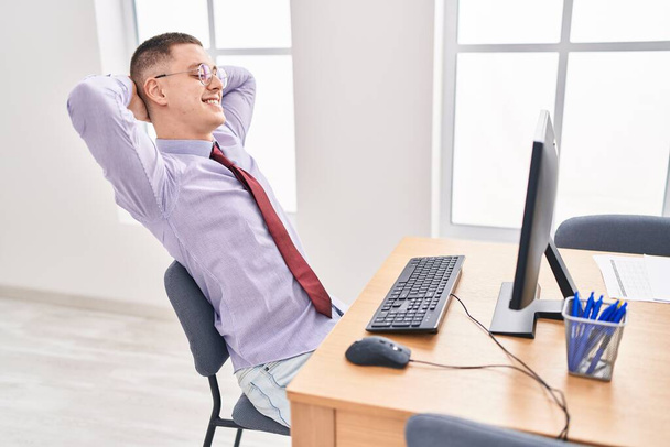 Jonge Spaanse man zakenman ontspannen met handen op het hoofd op kantoor - Foto, afbeelding