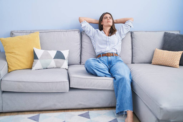 Young woman relaxed with hands on head sitting on sofa at home - Foto, immagini