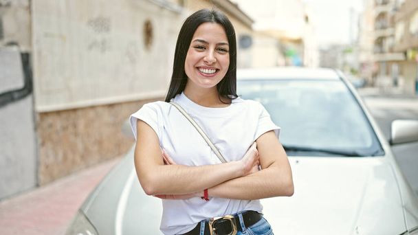 Young beautiful hispanic woman smiling confident standing with arms crossed gesture by car at street - Фото, зображення