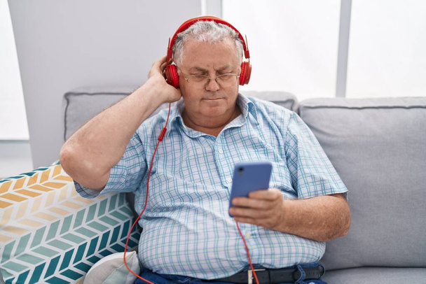 Średniowłosy mężczyzna słuchający muzyki siedzącej na kanapie w domu - Zdjęcie, obraz