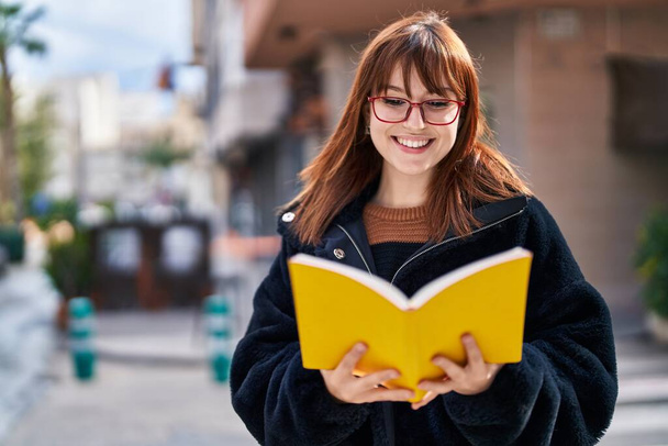Young woman smiling confident reading book at street - Photo, Image