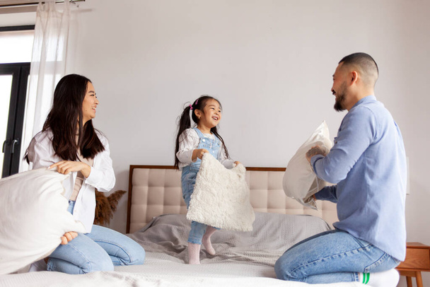 pillow fight, little Asian girl plays with her parents on the bed at home, Korean parents spend time with their daughter and rejoice, mom and dad have fun with the child - Fotoğraf, Görsel