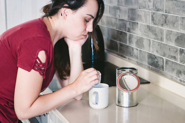 Mladá, bílá běloška, která ráno vypadá velmi unaveně ve své kuchyni a připravuje šálek čaje k snídani. - Fotografie, Obrázek