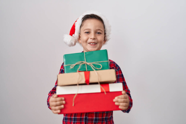 Mały latynoski chłopiec w świątecznym kapeluszu, trzymający prezenty, uśmiechający się i śmiejący głośno, bo śmieszny żart..  - Zdjęcie, obraz