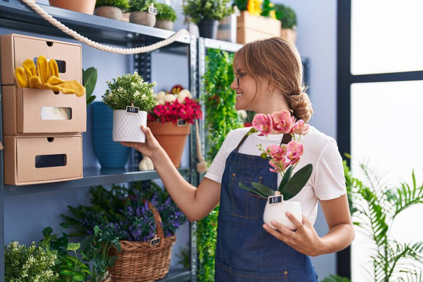 Giovane ragazza bionda fiorista sorridente fiducioso in possesso di vaso di piante al fiorista - Foto, immagini