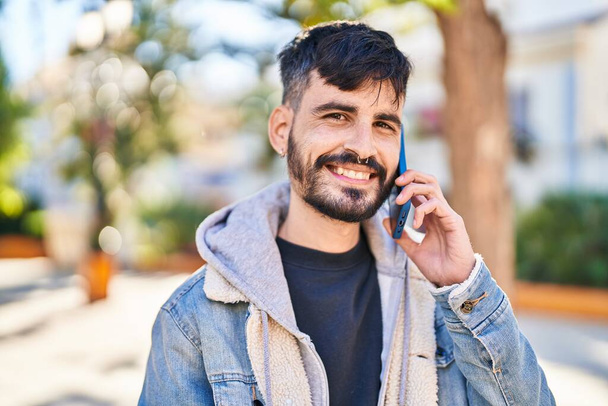 Νεαρός Ισπανόφωνος χαμογελά σίγουρος μιλώντας στο smartphone στο πάρκο - Φωτογραφία, εικόνα