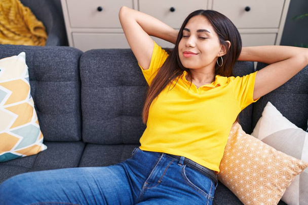 Young beautiful arab woman relaxed with hands on head sitting on sofa at home - Foto, imagen