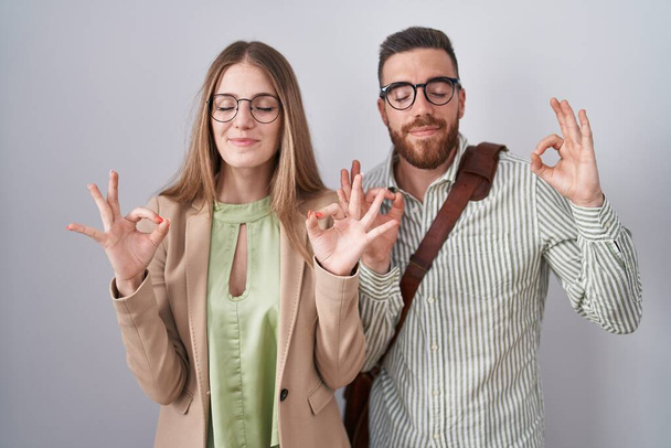 Young couple standing over white background relax and smiling with eyes closed doing meditation gesture with fingers. yoga concept.  - Valokuva, kuva
