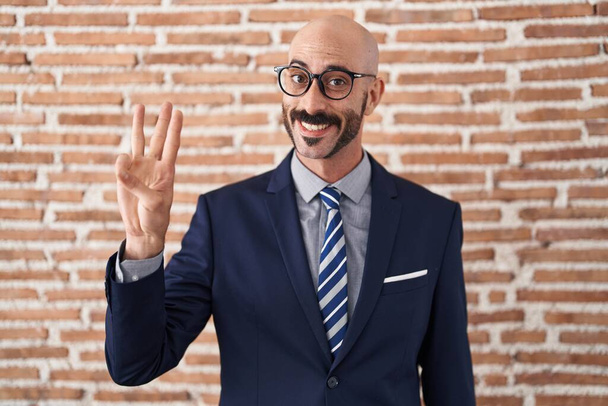 Kalju mies, jolla on parta yllään liikevaatteet ja lasit, osoittaa ja osoittaa sormella numero kolme hymyillen itsevarmana ja onnellisena..  - Valokuva, kuva