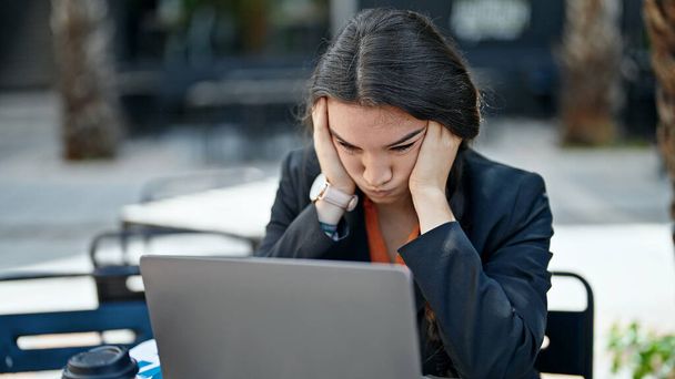 Fiatal gyönyörű spanyol nő üzleti dolgozó hangsúlyozta a laptop a kávézó teraszán - Fotó, kép