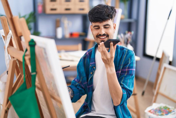 Νεαρός Ισπανός καλλιτέχνης μιλάει σε ένα smartphone ζωγραφίζοντας στο στούντιο τέχνης - Φωτογραφία, εικόνα
