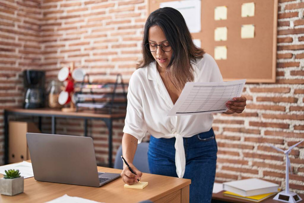 Jeune femme hispanique travailleuse d'affaires écrivant sur le papier de rappel tenant le document au bureau - Photo, image