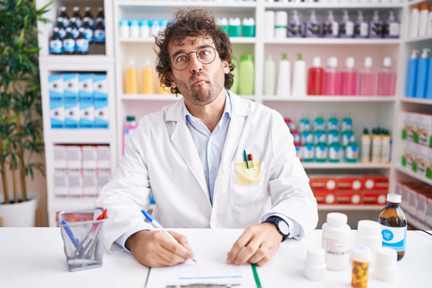 Spaanse jongeman werkt in apotheek apotheek drogisterij vissengezicht met lippen, gek en komisch gebaar. grappige uitdrukking.  - Foto, afbeelding